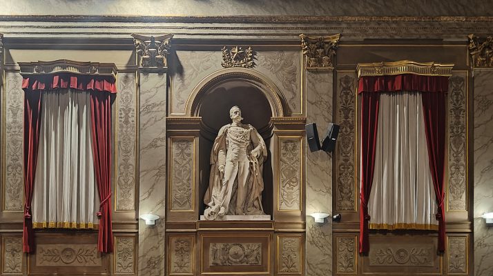 Statue in the consiliare hall with ornate decorations and red curtains at Palazzo Valentini.
