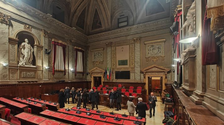 Interior of Sala consiliare at Palazzo Valentini in Rome, with ornate decorations and red seating.